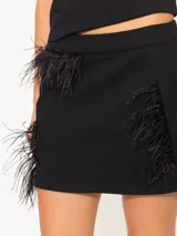 Minifalda negra de tejido de punto con corte ajustado a la cadera y detalle de plumas aplicadas en los laterales.