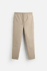 Pantalón de jogging color beige con cintura elástica ajustable con cordón, bolsillos laterales y traseros de vivo, y bajo con vuelta.