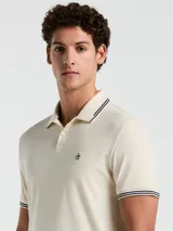Polo color crema con cuello clásico, mangas cortas y logo bordado en el pecho. Presenta detalles de doble línea en cuello y mangas.