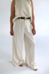 Pantalón de vestir color crudo, de corte palazzo y tiro alto. Presenta pinzas en la cintura y cierre frontal con botón y cremallera. Incluye cinturón trenzado marrón con hebilla redonda plateada.