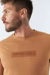 Remera color ocre de manga larga con cuello redondo y logo estampado en el pecho.