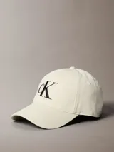 Gorra de béisbol color crema o blanco roto, confeccionada en algodón, con visera curva y bordado frontal grande del monograma 'CK' en color negro.
