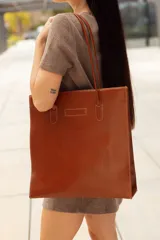 Bolso tote de cuero color marrón, con costuras a contratono y logo grabado en el frente.