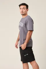 Bermuda deportiva gris de nylon, de corte suelto, con cintura elástica y cordón de ajuste. Cuenta con detalles de líneas negras en los costados y bolsillos laterales con cierre.