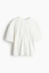 Remera larga color crudo, de punto pesado de algodón con cuello redondo y abertura en V en la espalda con tiras largas finas adornadas con dijes de cuentas brillantes. Modelo de hombros caídos con mangas amplias al codo y cintura entallada con pinzas adelante y atrás.