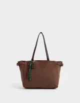 Bolso tipo shopper color marrón chocolate, de material símil gamuza, con doble asa corta de hombro, hebillas laterales y charm decorativo colgante.