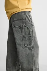 Pantalón color marrón con efecto lavado, corte relaxed fit, cinco bolsillos, aplicación de tira y bolsillo multifunción en perneras, cierre frontal con cremallera y botón.