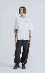 Remera blanca de manga corta con cuello redondo y calce oversize. Presenta una estampa en sublimación inspirada en el tarot, con la imagen de una figura femenina sosteniendo un salvavidas con la frase "Chill Bitch Trust Karma" y el texto "The Wheel of Fortune" en la parte inferior.