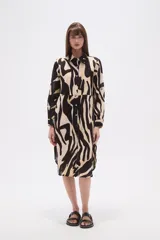 Vestido camisero midi holgado con estampado animal print tipo cebra en negro y beige. Presenta cuello camisero, botones frontales y mangas largas con puños abotonados.