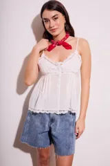 Blusa blanca de algodón con tirantes finos y escote en V. Presenta detalle de encaje en el escote y en el ruedo, y cierre frontal con botones.