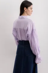 Camisa gris a rayas verticales blancas, de corte amplio, cuello alto con lazo y mangas largas abullonadas con puños elásticos.