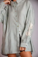Camisa celeste de corte clásico, con botones frontales y bordados florales en las mangas.