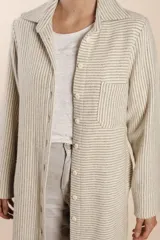 Camisa larga color crema con rayas verticales finas en gris, con botones dorados y bolsillo plaque en la delantera.