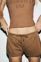 Shorts color marrón de algodón con efecto lavado, tiro medio, cintura elástica ajustable con cordones y detalle de tachas plateadas.