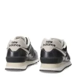 Championes New Balance modelo 574 Classics Traditionnels, color gris oscuro metalizado con detalles en beige claro. Presentan el logo 'N' en negro con borde beige y cordones color crema. La entresuela es beige con motas oscuras.