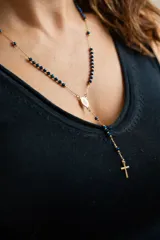 Collar estilo rosario con cadena dorada y cuentas pequeñas de color azul oscuro. Incluye un dije ovalado (medalla) y una cruz colgante en el extremo inferior.