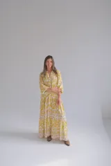 Vestido largo amarillo con estampado floral blanco, cuello en V, mangas 3/4 y corte escalonado.