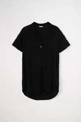 Vestido corto negro liso de manga corta, con cuello tipo solapa y escote en V con dos botones frontales. Presenta un corte recto y holgado, con bajo redondeado y más largo en la espalda.