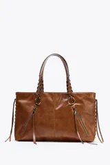Bolso shopper de hombro color marrón, con flecos y trenzados en el cuerpo. Tiene doble cremallera metálica, asa doble con detalles metálicos y trenzados, y bolsillo interior. Cierre mediante cremallera metálica.