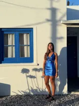 Vestido corto de fiesta color lila metalizado, con escote en V, breteles finos, cut-outs en la cintura y falda ajustada con cordones laterales.