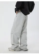 Pantalón deportivo gris jaspeado, corte ancho y holgado, con cordón ajustable en la cintura y detalle de etiqueta con texto en el bolsillo lateral.