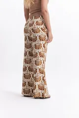 Pantalón wide leg estampado con diseño de conchas marinas color marrón sobre fondo blanco.