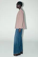Blazer color rosa palo, sin solapa, de corte recto y manga larga. Presenta bolsillos de ojal en el delantero y cierre frontal con gancho metálico.