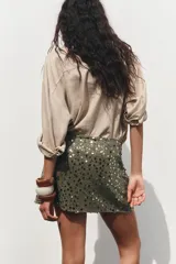 Falda pantalón verde militar con lentejuelas plateadas y negras, de tiro alto, con delantero cruzado y nudo.