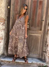 Vestido largo, con breteles finos y escote en V tanto adelante como atrás. Presenta un estampado de hojas en tonos marrón y beige sobre fondo rosado pálido.