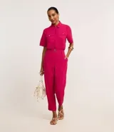 Camisa color beige de tela airflow, con cuello camisero, mangas cortas con detalle de pliegue, bolsillos con solapa en el pecho y cierre frontal con botones metalizados.