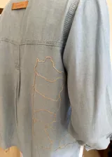 Camisa de denim combinado en dos tonos de celeste, corte holgado, con cuello clásico, mangas largas con puños abotonados, cierre frontal con botones y bolsillos de parche en el pecho.