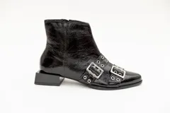 Bota corta de cuero charol color borgoña con punta fina y taco cuadrado negro. Presenta apliques de hebillas plateadas con ojalillos.