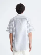 Camisa de manga corta con rayas verticales azules y blancas, cuello clásico y cierre con botones.