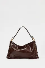 Bolso de hombro marrón oscuro con acabado brillante, asa trenzada y ojales metálicos en los laterales.