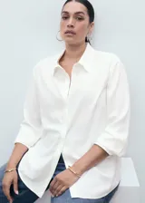 Camisa blanca de manga larga con puños abotonados, cuello camisero y cierre frontal de botones. Diseño recto con tejido fluido.