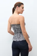 Top strapless (sin tirantes) de mujer, ajustado al cuerpo con efecto fruncido (smock) en todo el torso y un pequeño volante en el ruedo inferior. Presenta un estampado de cebra en blanco y negro.