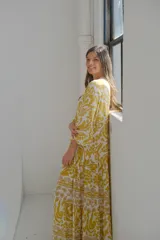 Vestido largo amarillo con estampado floral blanco, cuello en V, mangas 3/4 y corte escalonado.