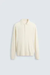 Polo de punto color crema, de corte regular fit, tejido en hilatura con mezcla de algodón y lyocell. Tiene cuello solapa con cierre frontal de botonadura, manga larga y acabados en rib.