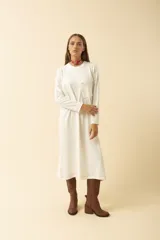 Vestido midi blanco de manga larga, con cuello redondo, bolsillo en el pecho y costuras a la vista.