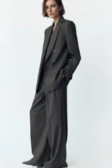 Pantalón gris de tiro alto con pinzas delanteras, bolsillos frontales y pernera ancha. Cierre frontal con cremallera, botón interior y gancho.