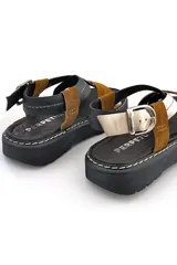Sandalias de cuero con tiras cruzadas color marrón, negro y dorado, con hebilla de ajuste y suela de goma negra.