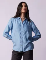 Camisa celeste de lyocell, con cuello a la base, escote en V y abertura central con botones. Tiene bolsillos aplicados en la parte delantera y mangas 3/4 regulables con presilla y botón.