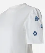 Remera blanca de algodón con cuello redondo, mangas cortas abullonadas y pequeños bordados florales azules en las mangas.