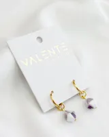 Aros Valente dorados con dije colgante de forma cúbica en color blanco y lila.