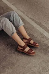 Sandalias de cuero marrón con tiras tejidas a mano y costuras a la vista, con base plana.