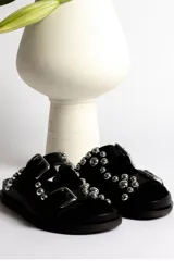 Sandalia tipo mule negra de cuero, con dos tiras ajustables con hebillas metálicas plateadas y apliques de tachas esféricas plateadas. Presenta un borde festoneado en la tira superior y suela de plataforma negra.