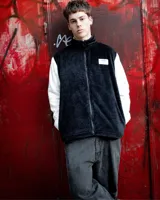 Campera de peluche negra con mangas largas color crema, cuello alto y cierre frontal. Presenta un parche con texto en el pecho.