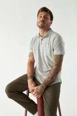 Pantalón chino color beige, de corte slim, con bolsillos laterales y traseros. Se ajusta a la cintura con cinturón de cuero marrón.