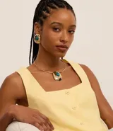 Conjunto de collar tipo gargantilla abierta y aros con tornillo, ambos con colgante y detalle de piedra de resina. El collar es dorado y tiene un dije con una piedra de resina turquesa y detalles en blanco y negro. Los aros son dorados con una piedra de resina turquesa.