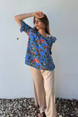 Blusa celeste con estampado floral en tonos naranja, verde y marrón. Tiene escote redondo y mangas cortas con volados.